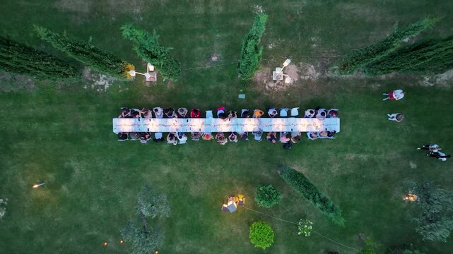 Aerial view of a long table set for a meal, surrounded by lush green grass and a few people, creating a warm gathering, Assisi, Umbria, Italy.
