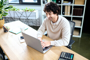 Bright young man working on laptop in modern office setting during daytime hours