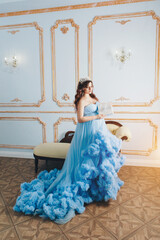 pregnant girl sitting on the floor in a lush blue dress. girl with dark hair wearing a crown.pregnant girl holding a gift. High quality photo