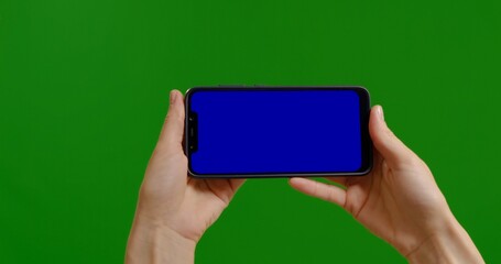 Female blue chroma key screen on smartphone device on green screen background. Woman phone in hands closeup watching something.