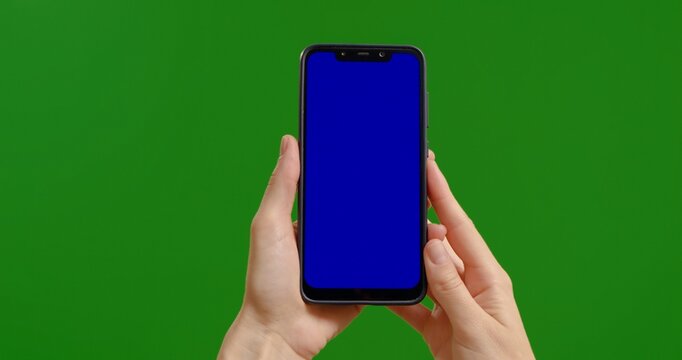 Female holds blue chroma key screen device vertically with fingers on green screen background. Phone user hands watch blue chroma key screen.