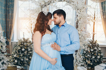man and woman bowed their heads to each other. a young pregnant girl in a lush festive blue dress and a young man in a blue shirt. man put his hand on pregnant woman's belly. expecting a child