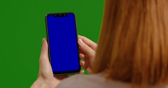 Woman taps blue phone chroma key while on green screen studio. Female hands using smartphone pausing video. - Powered by Adobe