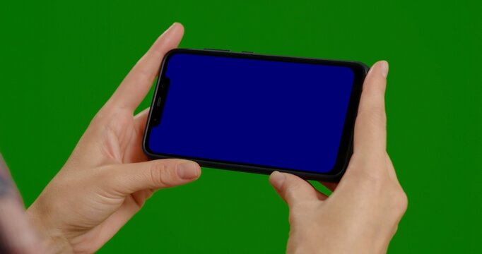Footage with woman hands holding blue screen phone over green screen background. Phone screen used for copy space advertisment. Technology addiction concept. - Powered by Adobe