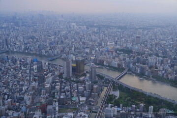 An expansive aerial view of a dense metropolitan city at dusk, with a wide river and multiple bridges crossing through it