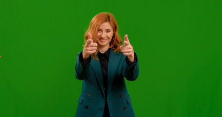Woman points at the camera both hands and smiles over green screen studio. Female happy by winning a prize.