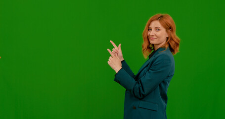 A woman with red hair is showing different gestures while standing against a green screen background. She appears confident and expressive, engaging in the activity.