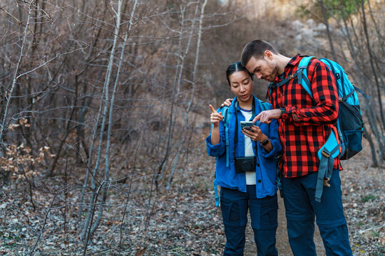 Young couple of hikers using smartphone gps application consulting map finding right path in forest during trekking day, sharing trekking path on social media
