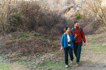 Interracial couple of hikers walking through forest trail enjoying scenic nature, talking to each...