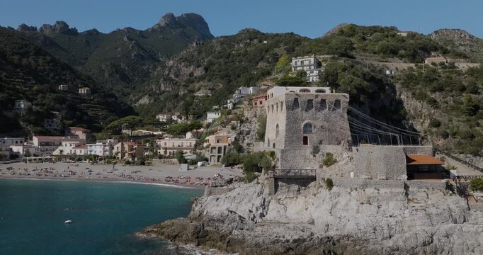 Aerial view of Torre La Guardiola's historic stone tower overlooking the beach with mountains in the background, Erchie, Amalfi Coast, Italy.