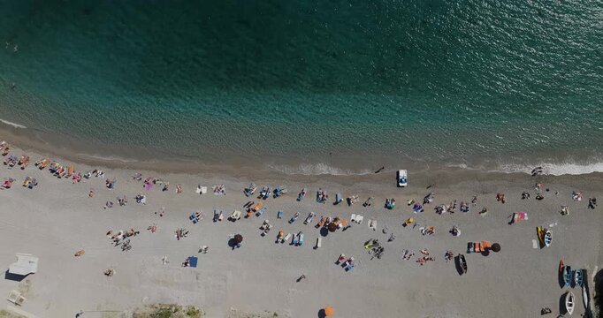 Aerial view of sunbathers dotting the sandy beach where the turquoise sea meets the shore in a stunning display of color and light, Erchie, Amalfi Coast, Italy.