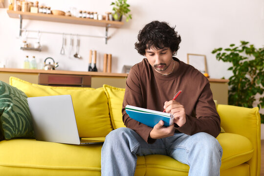 Fototapeta Young man writing notes while relaxing on a cozy yellow sofa in a bright living room