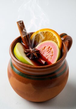 Hot Mexican Christmas punch, ponche navide&ntilde;o, in a traditional clay mug. Vertical photo of a festive winter drink with fruit, cinnamon, guava, and star anise on a white background