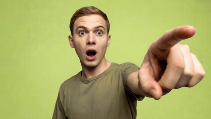 Shocked Young Man in a T-Shirt Pointing Emphatically Towards the Viewer or Side, With Wide Eyes and Open Mouth Against a Bright Lime Green Studio Background