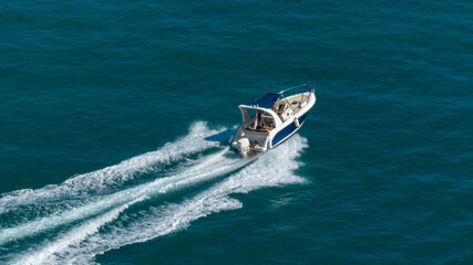 Aerial view of a motorboat sailing through the blue waters of the sea. As it passes, it leaves a white wake behind it.
