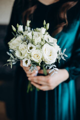 Woman in a teal dress holds a bouquet of white roses and greenery. The delicate composition conveys elegance, harmony, and a festive mood, highlighting the natural beauty of the moment.