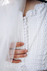 Close-up of a groom gently holding the bride in a white lace wedding dress. Elegant details of buttons and veil. Romantic and tender wedding moment.