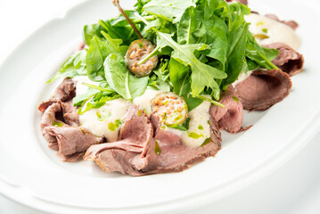 Vitello tonnato, a traditional Italian appetizer with thin slices of roast beef, creamy tuna sauce, and fresh arugula on a white plate.