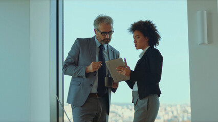 Diverse business professionals having an informal meeting, reviewing data on a digital tablet,...
