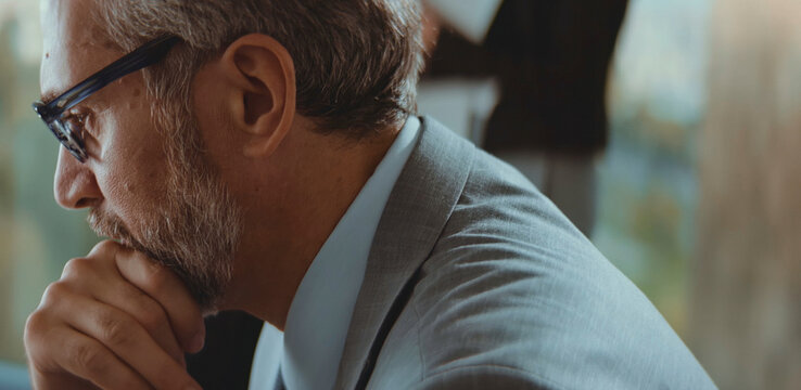 Thoughtful senior businessman with glasses and a beard, wearing a suit, intently focusing and contemplating a challenging idea or a complex problem in a professional setting