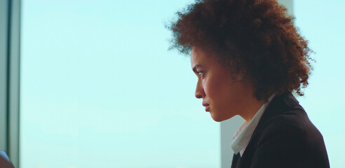 Young woman with natural curly hair and a determined expression focusing intently on her tasks, representing dedication and professionalism in a bright workspace