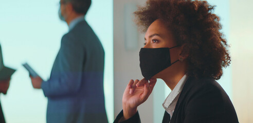 Young black businesswoman wearing a protective face mask while focusing on a presentation during a corporate meeting, adapting to new normal and health precautions