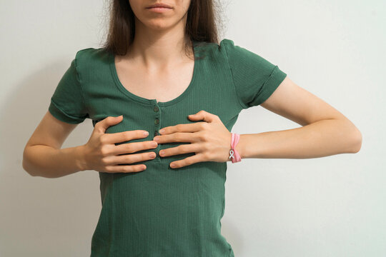 Woman in green shirt performing breast self-exam with pink ribbon bracelet