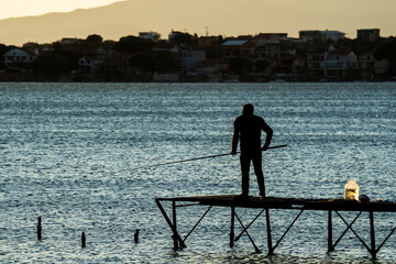 Silhouette of fisherman on pier at sunset by the sea