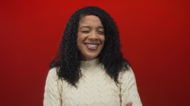 African american woman wearing cable knit sweater smiles with arms crossed in red studio; confidence warmth.