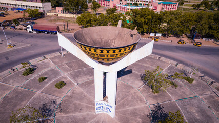 Aerial view of a large bowl-shaped monument standing proudly at the center of a roundabout, casting shadows on the textured pavement, Jippu Jam Roundabout, Adamawa State, Nigeria.