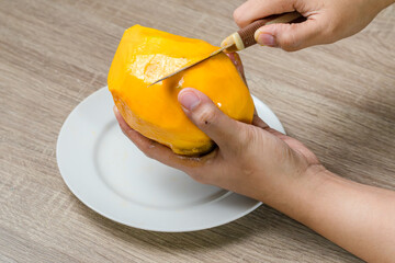 Hand holding a knife to peel and cut a mango fruit