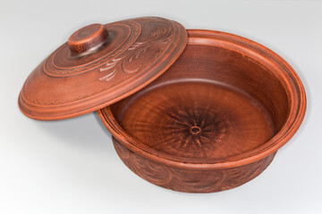 Round red clay roaster with shifted lid on gray background
