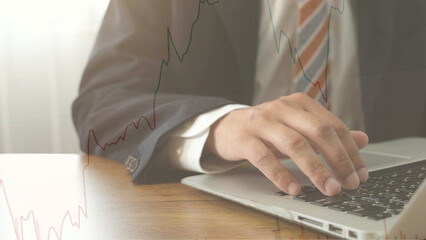 Businessman using laptop for financial analysis with stock market graph overlay, showing investment strategy and global economic trends in professional setting