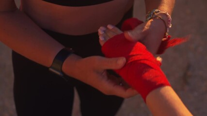 Coach wrapping female boxer's hand at beach during sunset, preparing for training. Close-up shot capturing the focus and dedication of the athlete and trainer in nature - Powered by Adobe