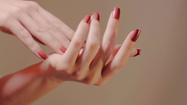 Hands gently clasp and release, displaying glossy ruby manicure and soft skin. Emphasizes detail, feminine grace and selfcare moments for lifestyle and spa. Fashion square shellac manicured nails