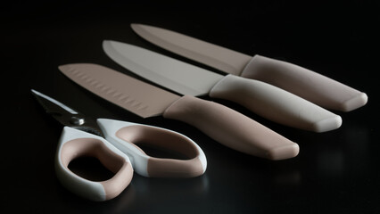 Modern pastel kitchen knives with silicone handles and color blades plus kitchen shears on a dark...
