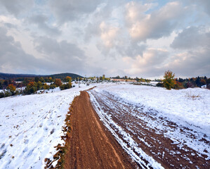 First winter snow on autumn mountain dirty road