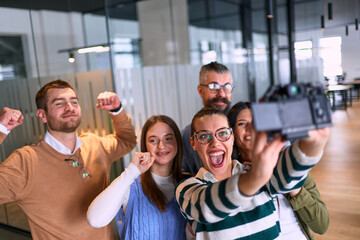 Group of cheerful coworkers taking a selfie together in a modern office environment. Concept of teamwork, friendship, success, and positive company culture.