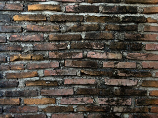A close-up, horizontal texture of an old, weathered brick wall with varying colors of red, brown, and black, set with rough mortar. Ideal for backgrounds and historical themes.
