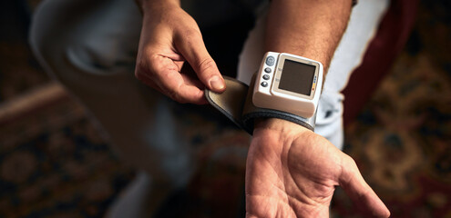 Man checking blood pressure and heart rate at home with a portable modern digital meter.