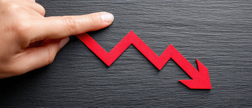 Economic slowdown concept with data showing decline trend in red arrow held by hand on black textured background