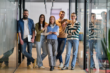 Group of young business team walking together through a modern office hallway, smiling and...