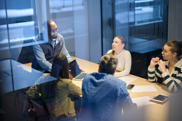 Diverse business team gathered around a table discussing analytics during a meeting in a modern office. Laptop screen shows charts and graphs, symbolizing teamwork, communication, and data driven