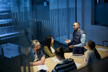 Diverse business team gathered around a table discussing analytics during a meeting in a modern office. Laptop screen shows charts and graphs, symbolizing teamwork, communication, and data driven