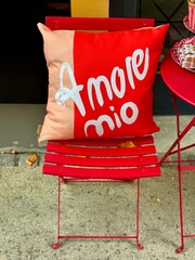 Red cushion with &ldquo;amore mio&rdquo; text on a red chair in outdoor cafe