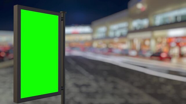 Green screen billboard standing by a blurred shopping street at night. Place your advertisement on the billboard with the provided chroma key