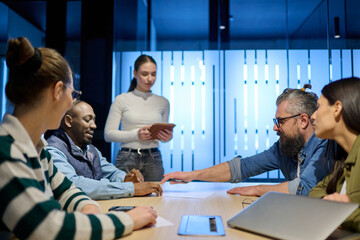 Diverse business team gathered around a table discussing analytics during a meeting in a modern office. Laptop screen shows charts and graphs, symbolizing teamwork, communication, and data driven