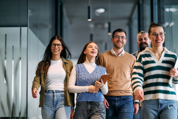 Group of young business team walking together through a modern office hallway, smiling and...