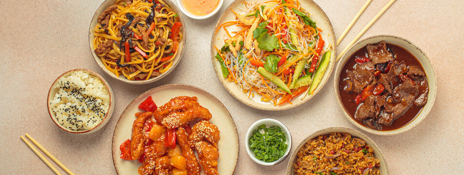 Assorted Chinese dishes, sweet and sour chicken, beef in sauce, noodles, fried rice, salad and wooden chopsticks. Chinese or Asian restaurant concept
