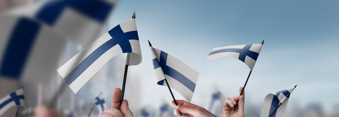 Finland flags in their hands on a blurred urban background